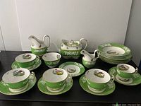 Full set arranged on table showing teapot, creamer, sugar bowl, cups, saucers and plates with white and green coloring, painted bird motifs and gilt edging.