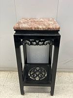 Front view of the black lacquered wood pedestal table with marble top, showing carved apron and lower shelf detail.