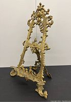 Side angle of the detailed antique brass picture easel showing ornate scroll design and feet.
