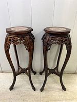 Front view of both pedestal tables showing octagonal marble tops and carved wood bases