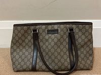 Front view of tote on carpeted floor showing full GG monogram canvas and leather straps