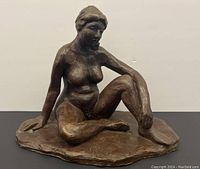 Front view of cast bronze seated nude woman sculpture showing full figure and base.
