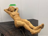 Full view of the reclining nude woman sculpture on a black carved wooden surface showing the pose and proportions