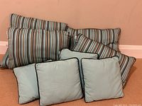 Photo showing set of 10 outdoor pillows including large striped pillows in turquoise and brown, medium striped pillows with piping, and small solid turquoise pillows with piping.