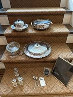Photo showing all silver plated serving pieces and frames arranged on stairs including covered dishes with Pyrex liners, salt and pepper shakers, spoons, and frames