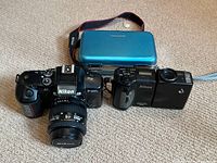 Nikon F-401X with Nikkor lens and Coolpix 950 digital camera alongside blue Vanguard camera case on carpet.