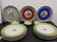 Overview photo showing all three decorative cabinet plates in jewel tones alongside two stacks of pale green border Hutschenreuther dinner plates and four small bowls.