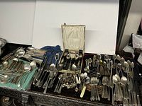 Overview of large silver plated cutlery lot arranged on table with various types of forks, spoons, and serving tools spread out, some in cloth wraps.
