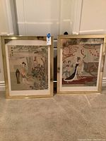 Two framed oriental style art prints shown side by side on carpet against white wall