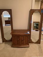 Photo showing one wood nightstand with curved front and two doors, flanked by two tall wood-framed wall mirrors with arched tops