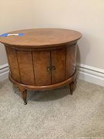 Closed view of circular wooden storage cabinet side table showing round tabletop and double doors with metal handles.