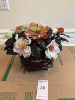 Full view of stone flower arrangement on carved wooden base showing variety of flower colors and shapes.