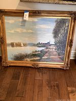 Overall view of framed painting showing water, sailboats, pathway and village under a sky