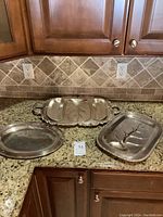 Three silver on copper serving trays on granite countertop with tile backsplash.