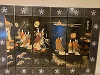 Front view of six-panel folding screen showing traditional Oriental figures and decorative border patterns in black lacquered panels.