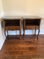Front view of two matching wooden nightstands with glass tops and single drawers.