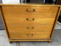 Front view of 4-drawer wooden dresser on rectangular base with brass-tone handles