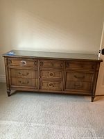Front view of wood dresser with nine drawers and clear glass top, showing drawer details and wood finish under natural light.