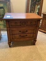Front view of wooden nightstand showing three drawers and decorative carving on top drawer.