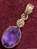Close-up photo of the 14K gold pendant showing the oval amethyst and the round diamond above it on a burgundy background.