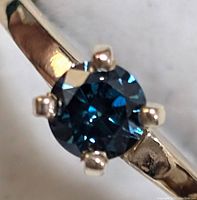Close-up front view showing round blue diamond and six-prong setting