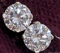 Front view of both stud earrings on burgundy fabric showing diamond size and sparkle