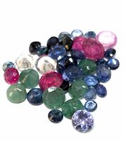 Loose gemstones grouped together, showing various colors and cuts of emerald, ruby, and sapphire.