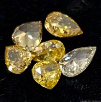 Six loose fancy color diamonds in yellow and clear shades, pear and trillion cuts, displayed on black background.