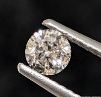 Close-up photo of the salt and pepper diamond held by tweezers showing detailed inclusions.
