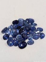 Photo showing a pile of loose faceted blue sapphires in various shades and oval shapes.