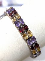 Close-up angled view of the sterling silver bracelet displaying the prong-set garnet, amethyst, and citrine stones arranged in three rows.