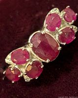 Close-up photo showing sterling silver ring with oval and round faceted ruby gemstones.