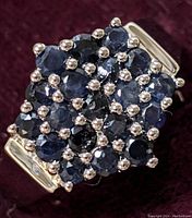 Close-up of ring top showing multiple round blue sapphires set in sterling silver with prongs.