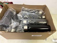 Box containing 18 black bottles with silver caps, still wrapped in plastic.