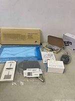 Wide shot of computer accessories lot showing wireless keyboard box, blue wrapped keyboard or device, HDMI adapters, AC adapter, docking station, and assorted cables.
