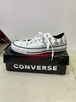 Side profile of white low-top Converse sneaker with multiple Bugs Bunny images printed on the outer side, placed on a damaged black Converse branded shoebox.