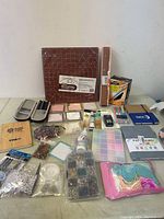 Lot contents including cutting mat, bead organizer, sticky notes, colored markers, password book, strings, and other stationery items laid out on table.