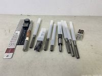 Wide view of drill bits and milling cutters with protective tubes along with two AA batteries and a digital angle ruler