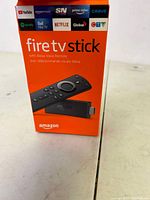 Box of Amazon Fire TV Stick showing front side with logos of supported streaming services and an image of the remote and device.
