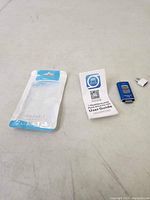 Photo showing the empty USB cable packaging, user guide, blue flash drive, and USB adapter laid out on a table.