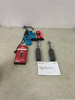 Gaming accessories arranged on table including Nintendo Switch Joy-Con controllers with straps, Mayflash NS adapter boxed, and PlayStation Camera Adapter with manual.