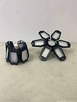 Two garage LED lights with multiple foldable panels placed on a flat surface revealing design and structure.