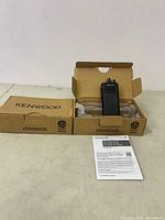 Overall view of two Kenwood radios in original Kenwood boxes with user manual on table.