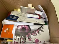 Top-down view into large box showing multiple notebooks, pads and stationery items packed inside.