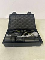 Open carrying case showing black rechargeable flashlight with side button, USB cable and lanyard inside foam insert.