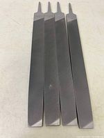 Top view of four new metal rasp files, showing smooth backs and tapered blades.