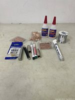 Photo showing various welding accessories arranged on table including adhesive bottles, copper tips, solder wire spool, and markers.
