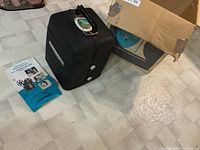 Photo showing the black plastic carrying case with handle, instruction manual laid next to the case.