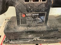 Close-up photo of the label on the Black & Decker sander showing model description as 1/3 Sheet Variable Speed Sander with Dust Extraction