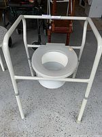 Front view of white metal frame commode with removable plastic pot and adjustable height legs.